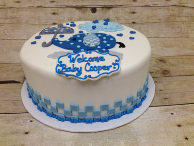 white fondant icing baby shower cake with blue spotted elephant holding an umbrella on top.