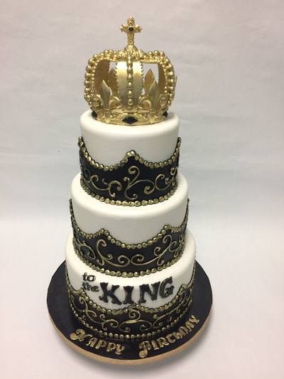 3 tier happy birthday cake with kings crown on top. black and gold scroll work.