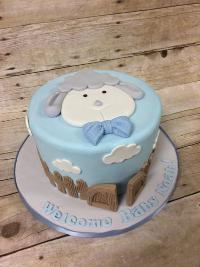 boys baby shower cake with lamb face on top and clouds and a fence around the outside of cake.