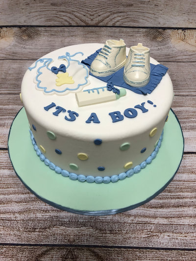 it's a boy baby shower cake. chocolate baby boots, and bib and a bottle on top. blue yellow and light blue dots around the ooutside.