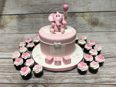 single tier baby shower cake with elephant on top and blocks in front surrounded by pink frosted cupcakes.