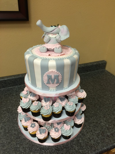 Girls baby shower cake. With baby girl elephant on top colors are pink grey and white with matching cupcakes.