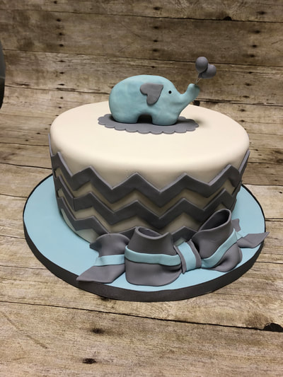 baby shower cake, light pink with blue elephant holding balloons and wavy fondant stripes around the outside. 
